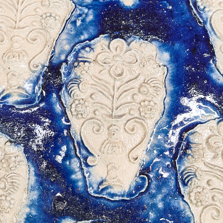 Keramikkachel mit Blumenornamenten in hellen Beige- und Blau-Tönen, mit detailreichem reliefartigem Blumendesign und glänzender glasierter Oberfläche.