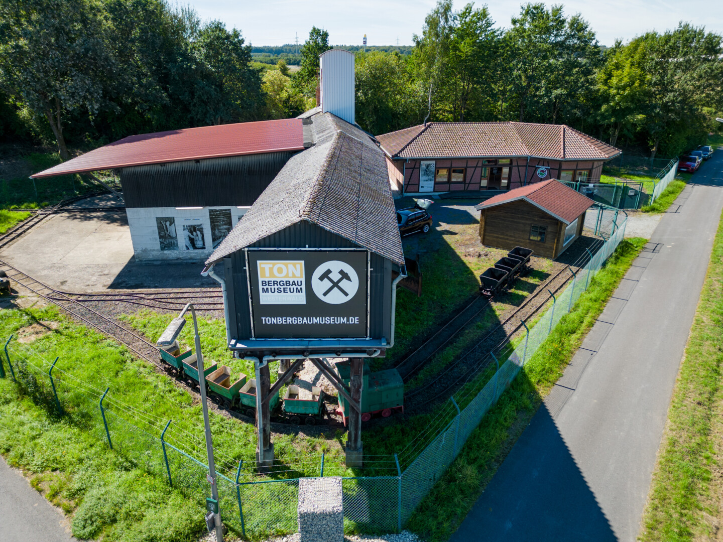Tor zum Tonbergbau Museum Westerwald mit kleinen Loren auf Gleisen und mehreren Gebäuden in ländlicher Umgebung